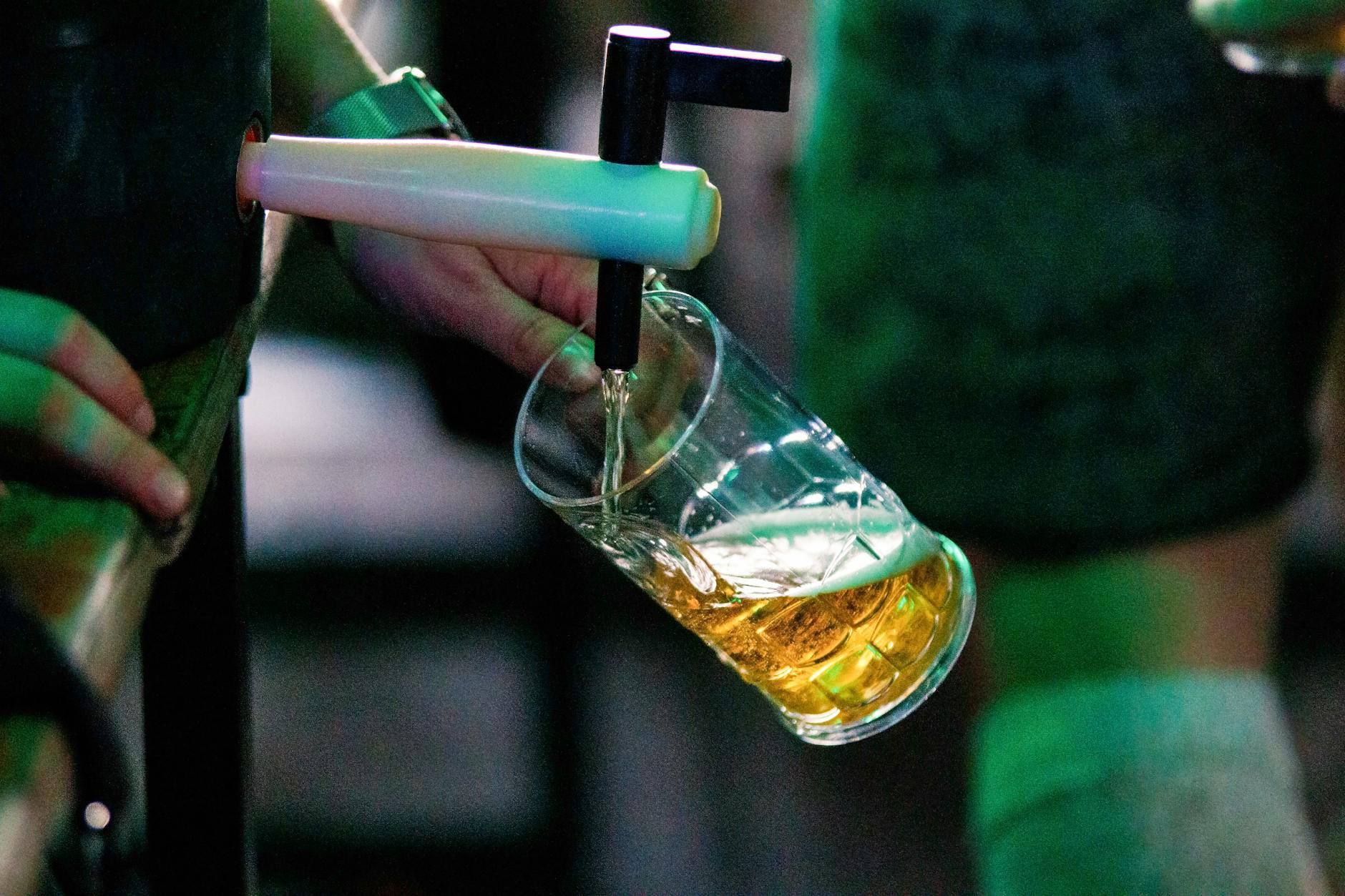 Close-up of a person pouring beer from a tap into a glass at a bar.