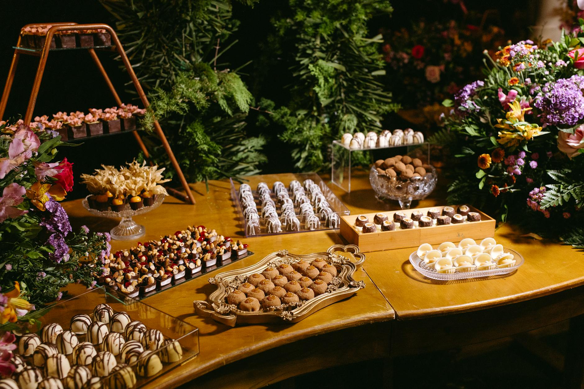 A beautifully arranged dessert table featuring assorted chocolates and pastries, surrounded by floral decorations.
