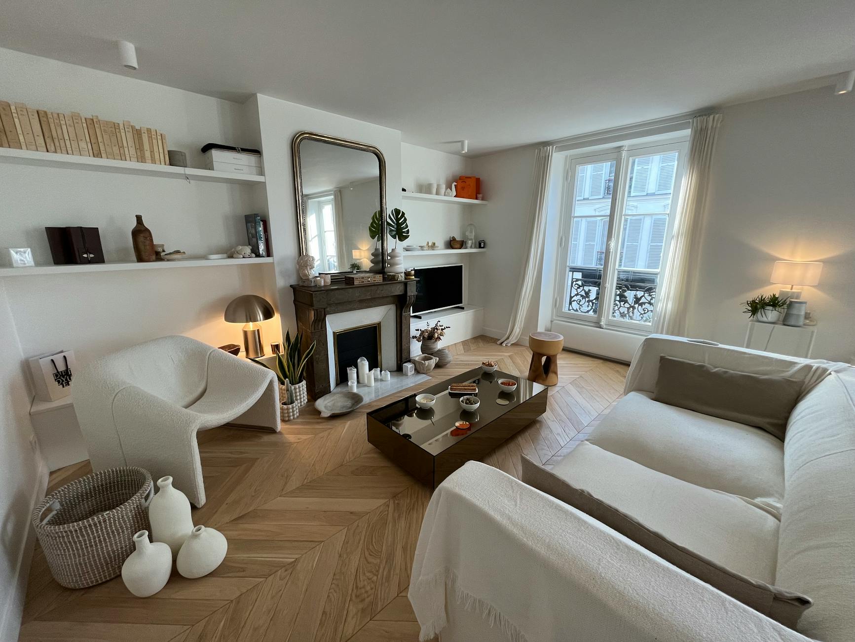 A cozy modern living room with chic decor, light tones, and a central fireplace.