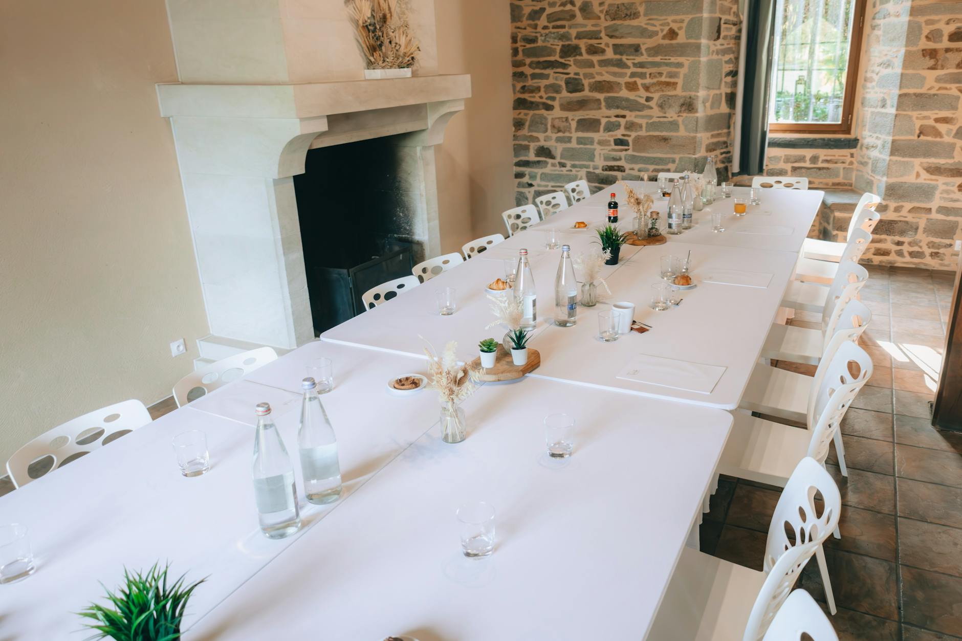 Charming dining table with bottles, plants, and decor in a rustic stone-walled room.