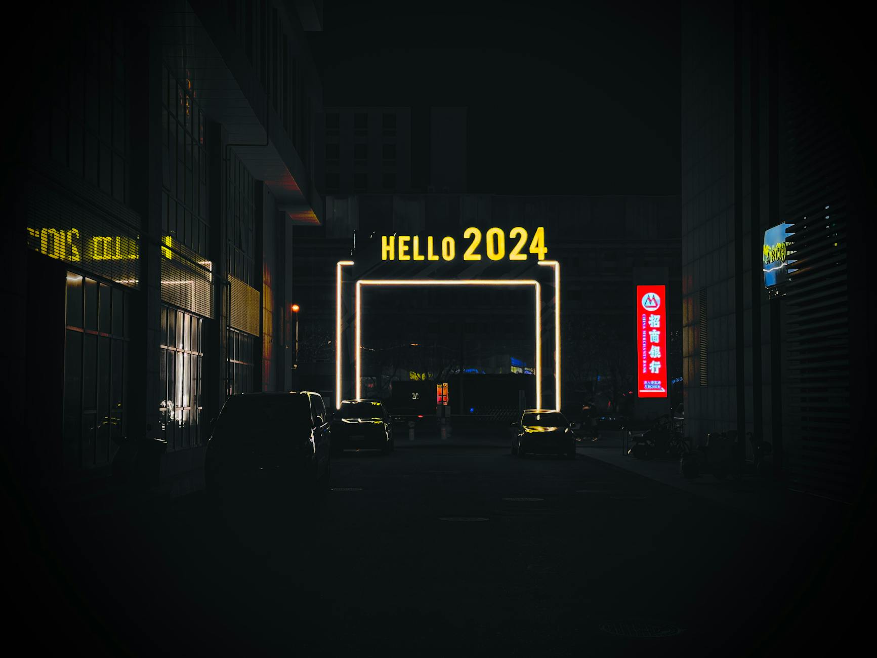 Urban night scene features an illuminated 'Hello 2024' sign in a bustling city alleyway.