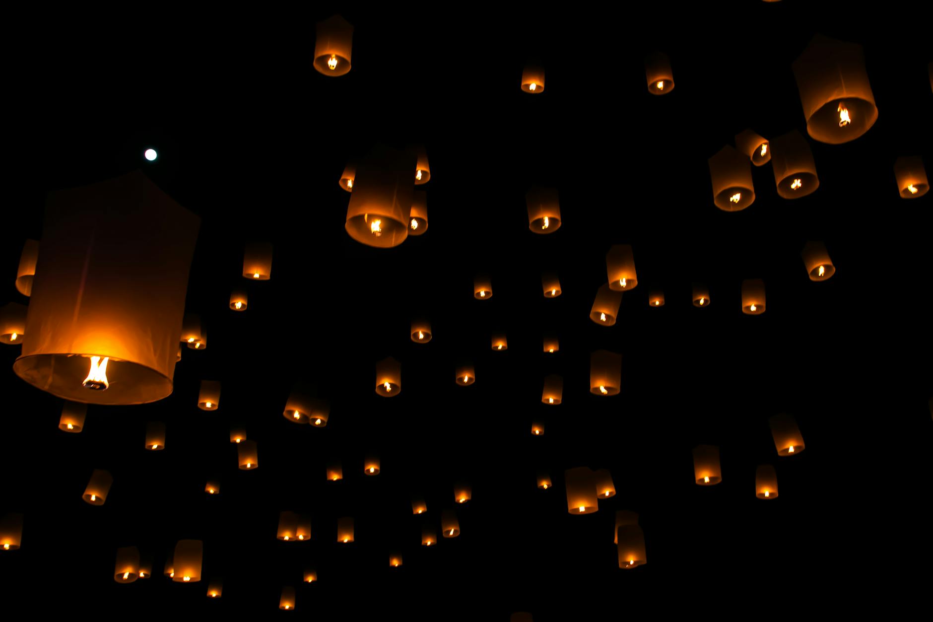 Sky lanterns float against a dark night sky during a traditional festival in Thailand.