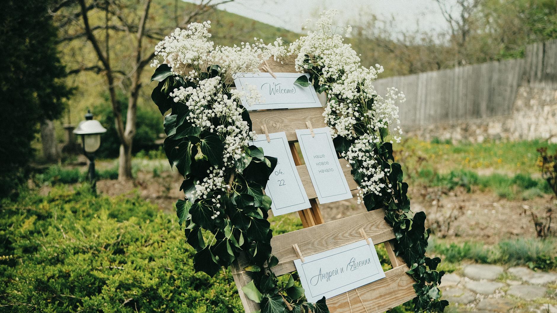 Wooden wedding sign adorned with ivy and Gypsophila in a garden setting.
