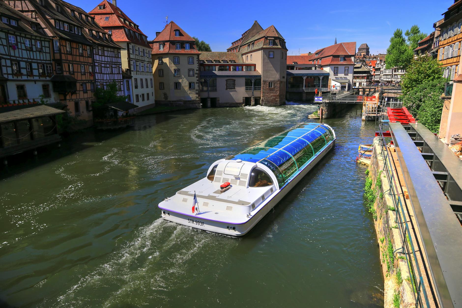 A modern boat sails through the historic canals of Strasbourg, showcasing traditional Alsatian architecture.