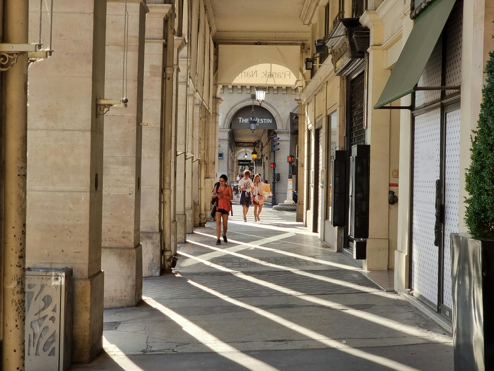 Sunlit passageway in Paris with people walking. Summer day, The Westin Paris Vendôme hotel.