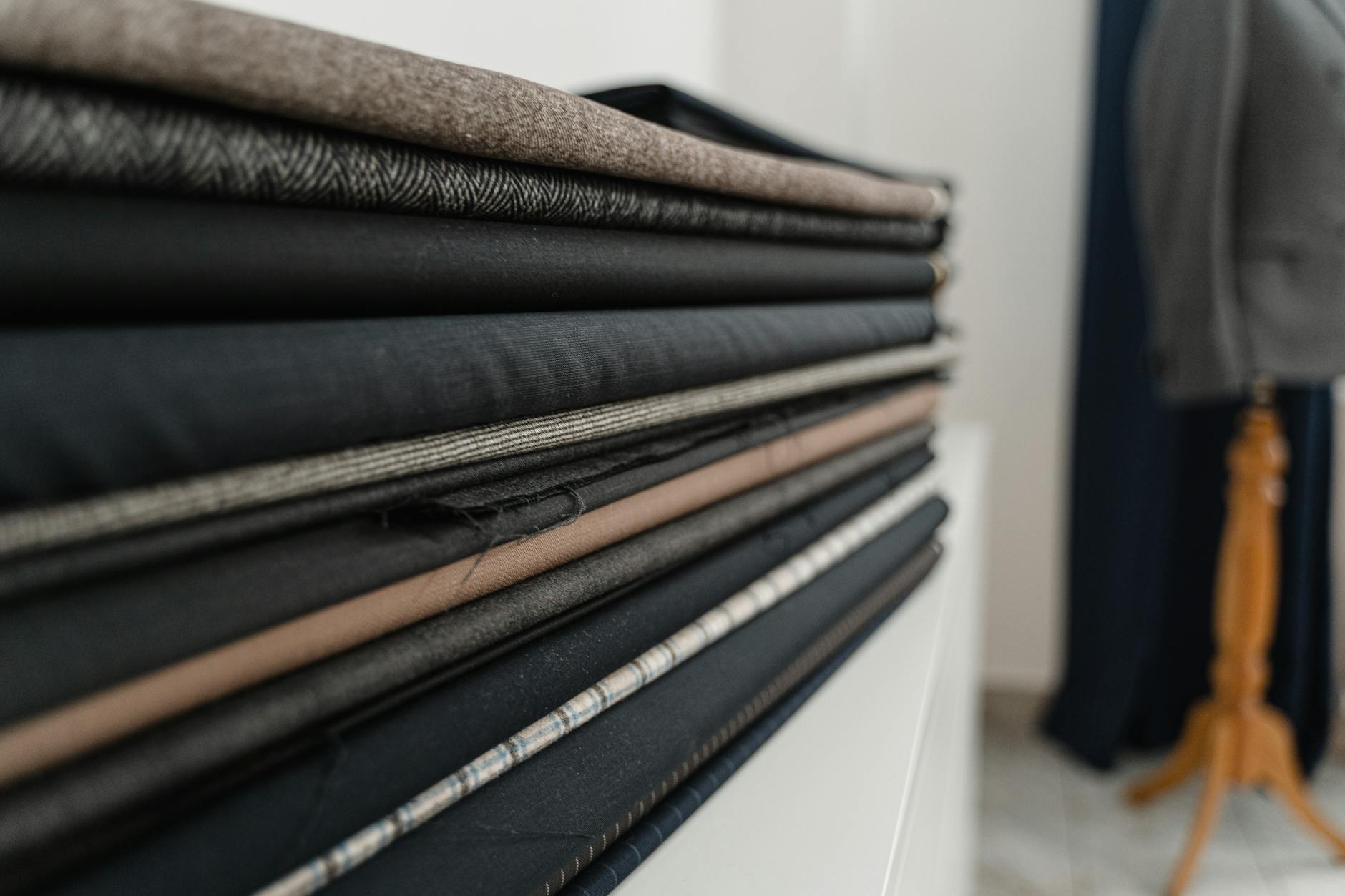 A stack of various folded fabrics in a tailor shop, showcasing texture and color variety.