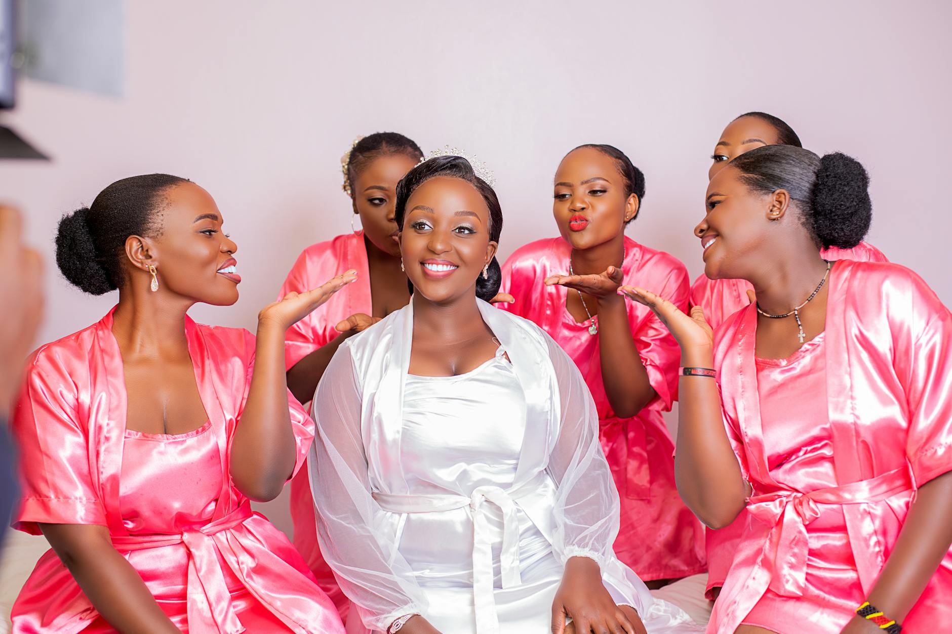 Joyful bridal party wearing pink robes, celebrating and smiling indoors.