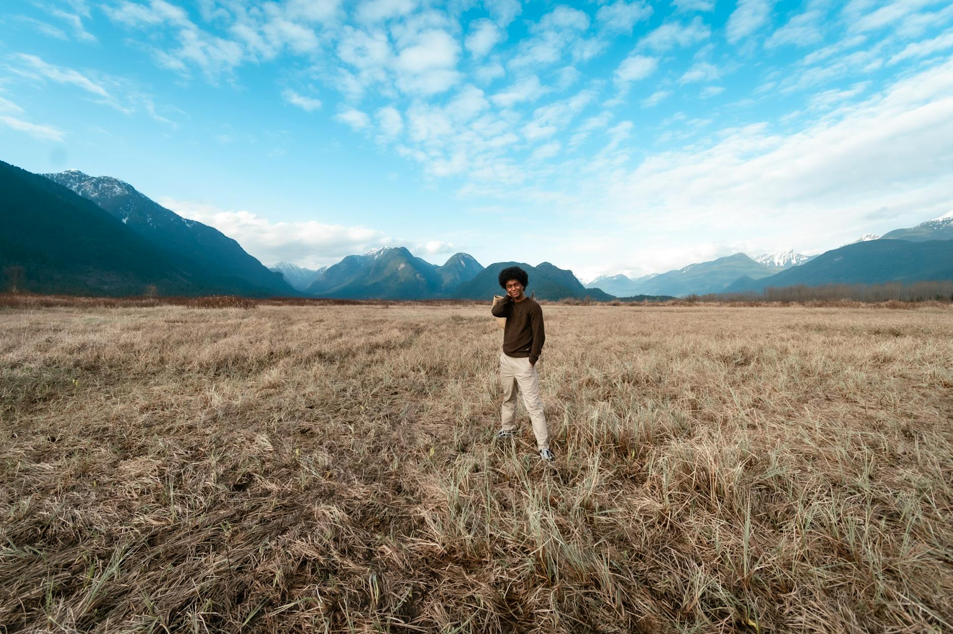 A person in a grassy field with majestic mountains under a blue sky.