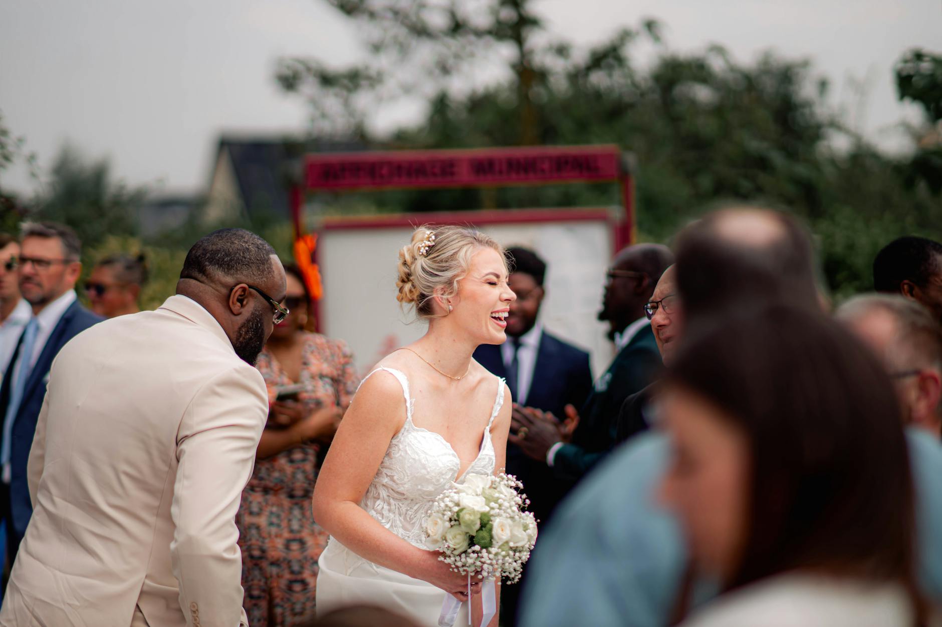A bride smiling amidst guests at an outdoor wedding ceremony. Celebration and happiness.